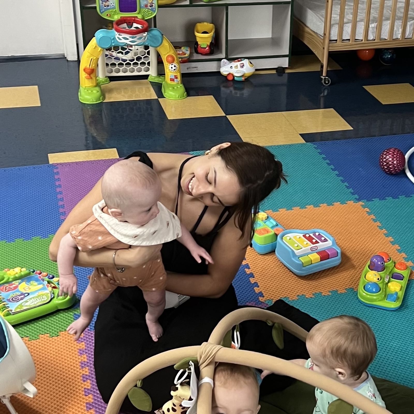 Mrs. Gaby smiling down at a baby she is holding on the play mat