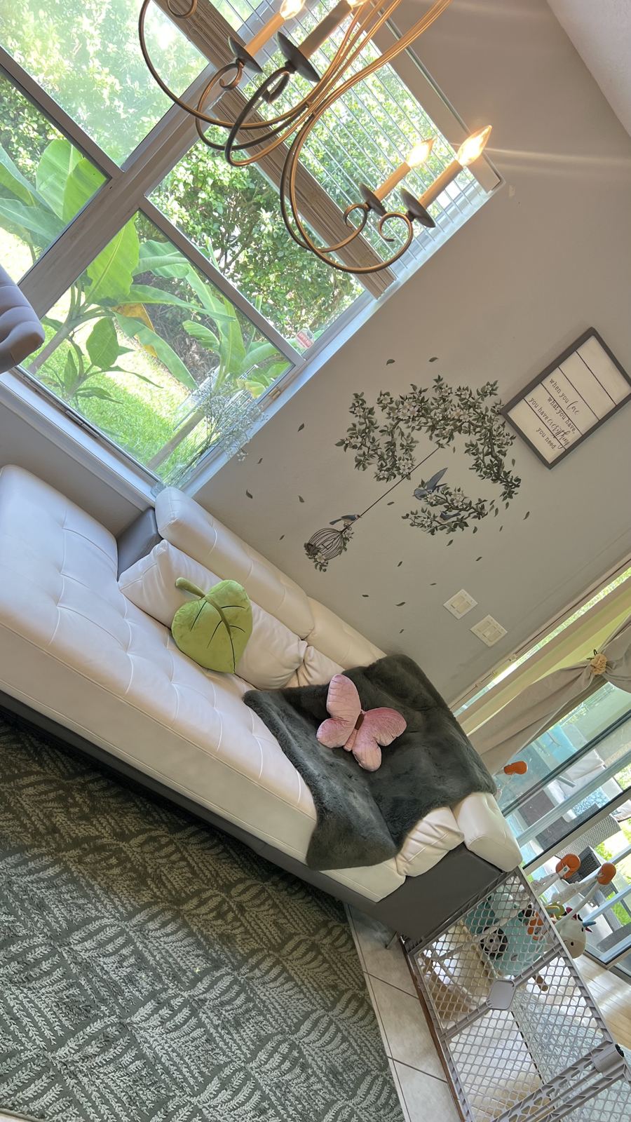 Sunlit family room with tall windows, a soft sofa, and a safety gate at the stairs